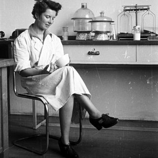 Woman in lab coat seated, holding a flask.