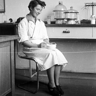 Woman in lab coat sits in a laboratory setting.