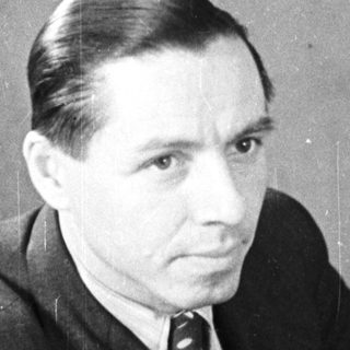 Man in a suit sits near a wooden door.