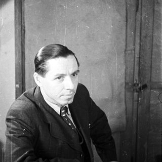 Man in a suit sits near a wooden door.