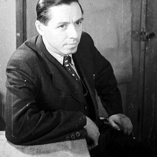 Man in a suit sits near a wooden door.
