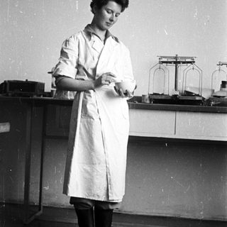 Woman in lab coat stands near laboratory equipment.