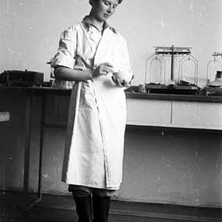 Woman in lab coat stands near laboratory equipment.