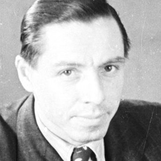 Man in suit sits near a door, looking directly ahead.