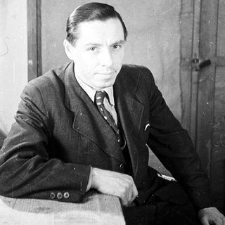 Man in suit sits near a door, looking directly ahead.