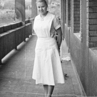 Woman stands on a porch with a wooded backdrop.