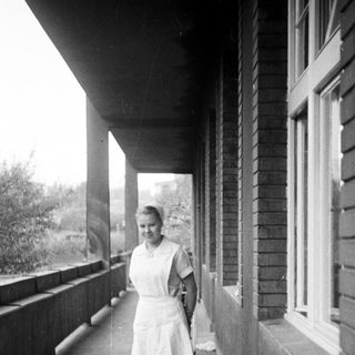 Woman stands on a porch with a wooded backdrop.