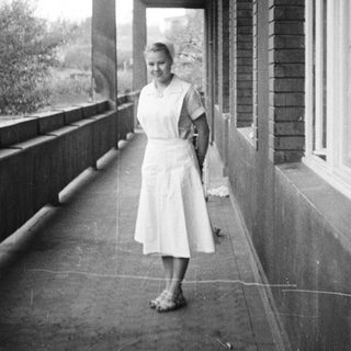 Woman stands on a porch with a wooded backdrop.