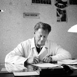 Man in lab coat writing at a desk.