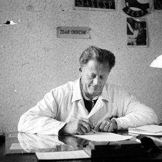 Man in lab coat writing at a desk.