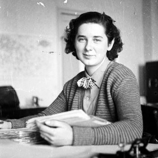 Woman smiles at camera while seated at a desk.