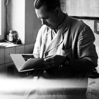 Man in lab coat reading a book at a table.