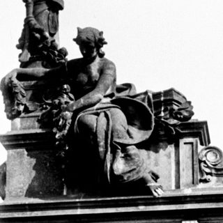 Here's a brief summary of the image: Monumental statue atop a building, viewed from below.