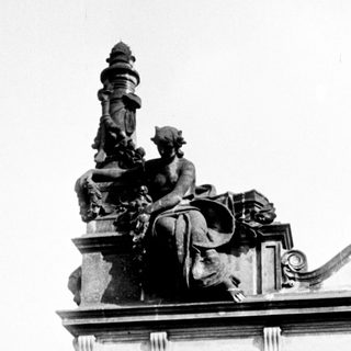 Here's a brief summary of the image: Monumental statue atop a building, viewed from below.