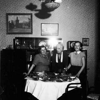 Here's a brief summary of the image: Three people stand behind a table with food.