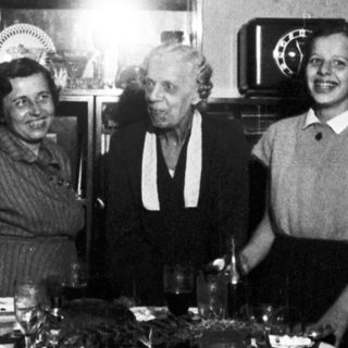 Here's a brief summary of the image: Three people stand behind a table with food.