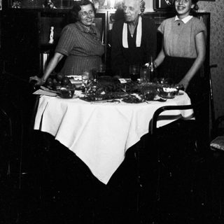 Here's a brief summary of the image: Three people stand behind a table with food.