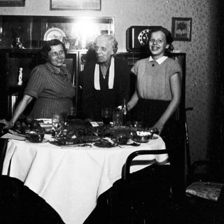 Here's a brief summary of the image: Three people stand behind a table with food.
