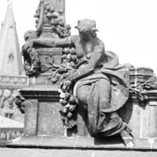 Statue and spire view through an arched stone structure.