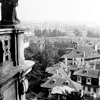 Statue overlooking a city with rooftops and distant buildings.