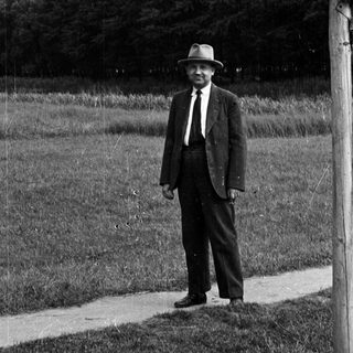 Man in a suit and hat stands near a path.