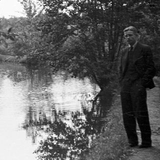 Man stands near a river surrounded by trees.