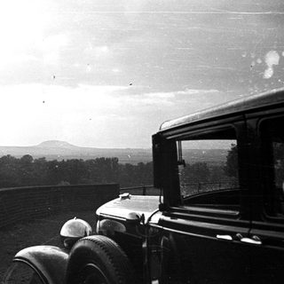 Vintage car overlooks a landscape with a distant hill.