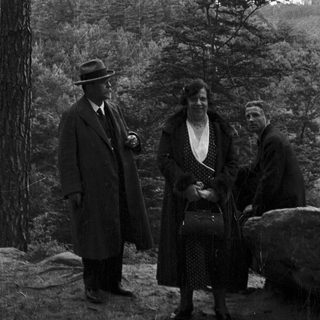 Three people pose near a castle in a wooded landscape.