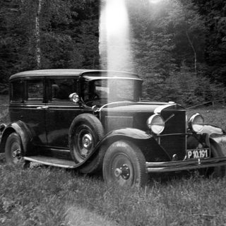 Vintage car parked in a grassy, wooded area.
