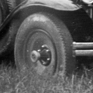 Vintage car parked in a grassy, wooded area.