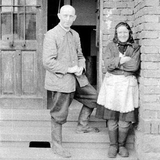 Couple standing on porch steps in vintage clothing.
