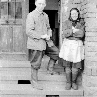Couple standing on porch steps in vintage clothing.