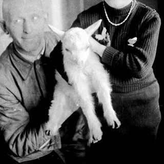 Man and child holding a young goat indoors.