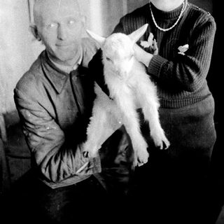 Man and child holding a young goat indoors.