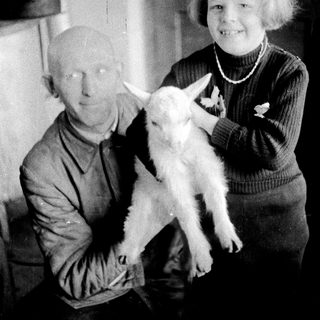 Man and child holding a young goat indoors.