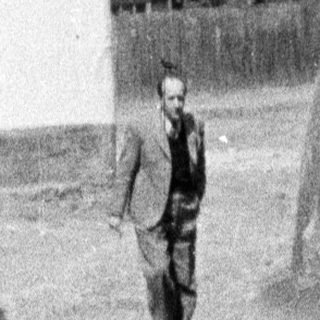 Men walk past a tower and building.
