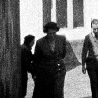 Men walk past a tower and building.