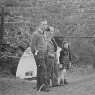 Group of people standing near a stone wall and door.