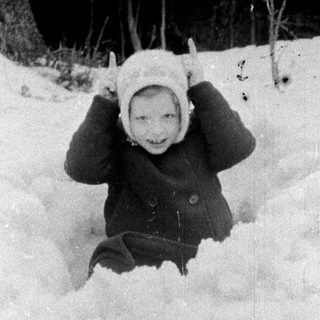 Child playing in snow, wearing a hat and coat.
