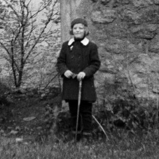 Man stands before stone ruins, holding a walking stick.