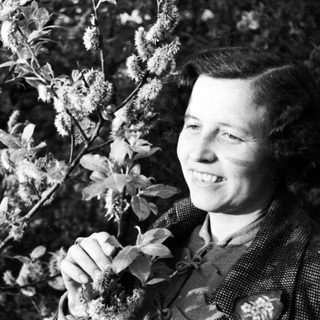 Woman smiles next to a willow tree in black and white.