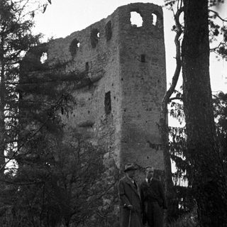 Ruined tower with men standing nearby, overgrown with vegetation.