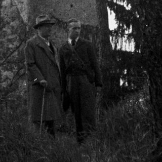 Ruined tower with men standing nearby, overgrown with vegetation.