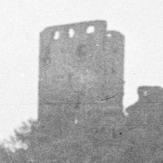 Ruined castle on a hill, surrounded by trees.
