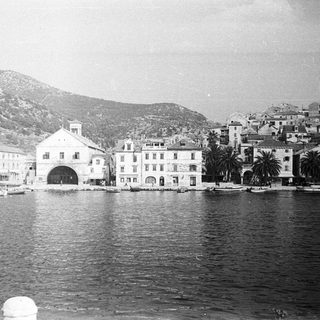 Coastal town with buildings, boats, and mountains in background.