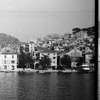 Coastal town with buildings, boats, and mountains in background.