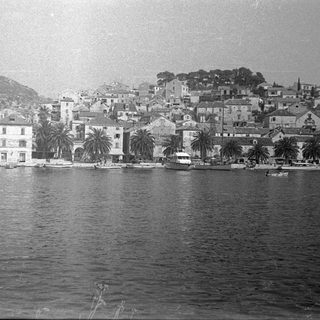 Coastal town with buildings, palm trees, and boats on water.