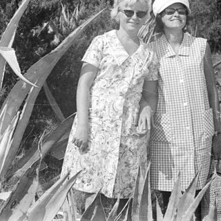 Two women stand outdoors, dressed in vintage clothing.