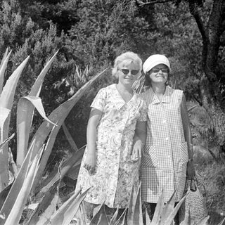 Two women stand outdoors, dressed in vintage clothing.
