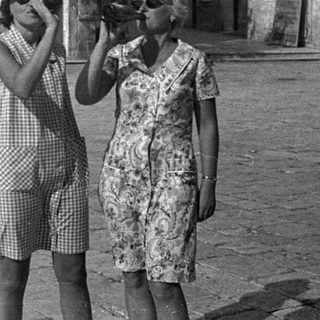 Two women looking through binoculars in a town square.